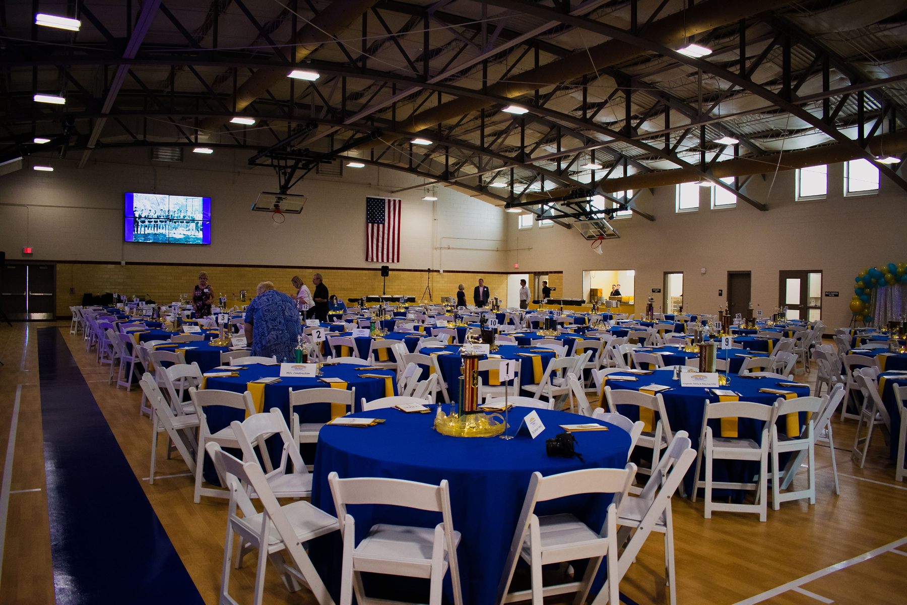 The field house set for a banquet — round tables in blue and gold linens with white folding chairs across the gymnasium floor